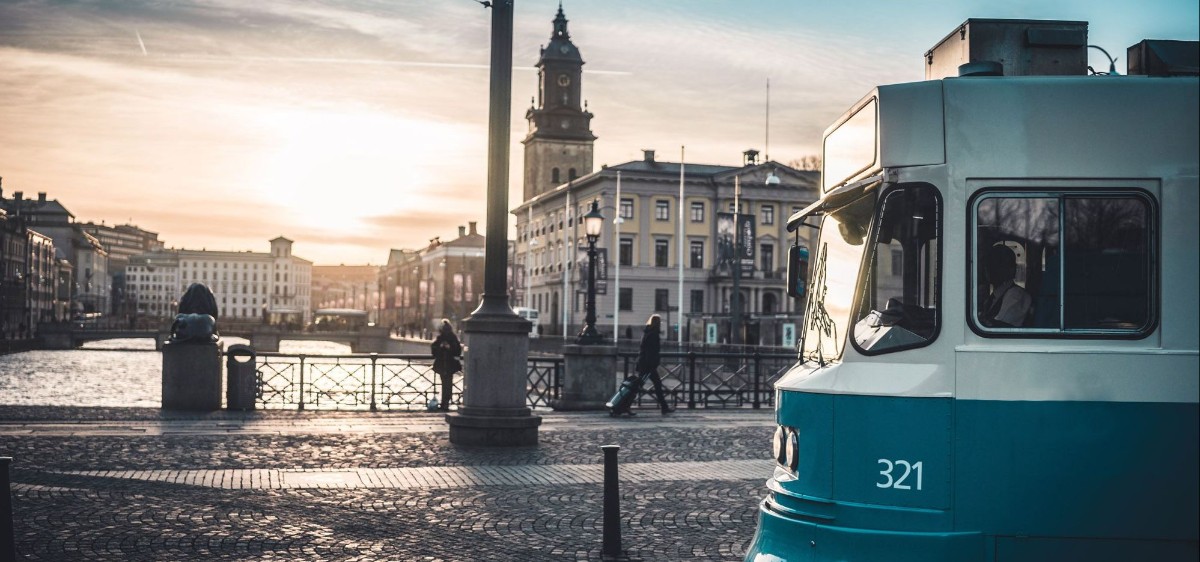 Spårvagn åker in i bild från höger. I bakgrunden syns en solnedgång över en stad