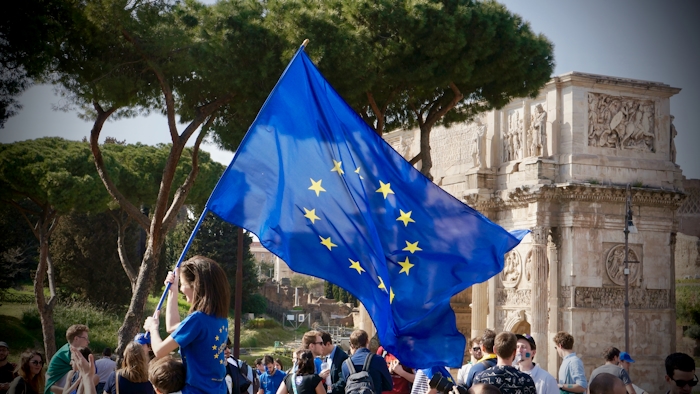 Flicka håller en EU-flagga i en folkmassa, i bakgrunden syns träd